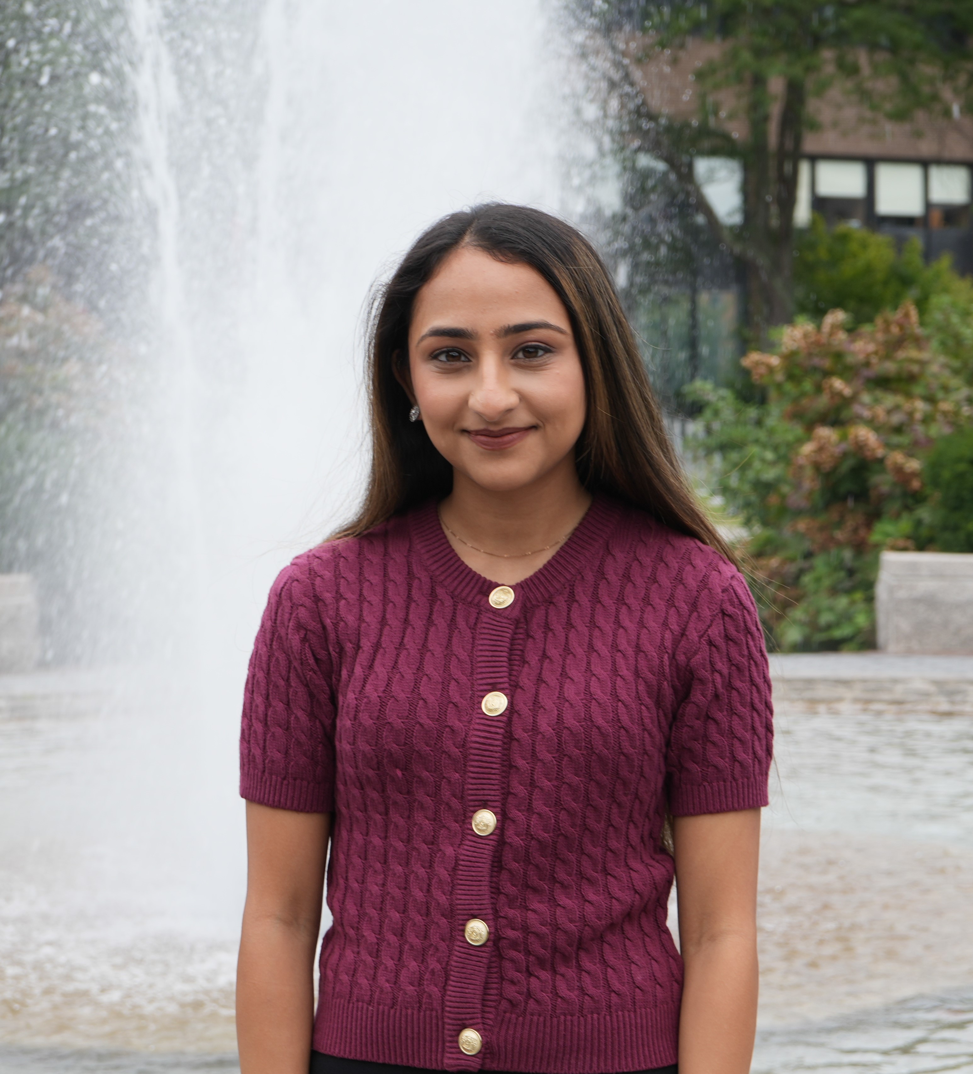 Person in a burgundy sweater standing in front of a fountain.