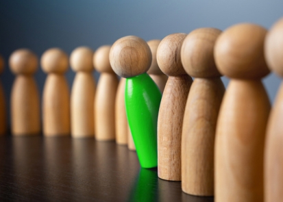 A line of people-shaped blocks with one painted green and tipped forward slightly