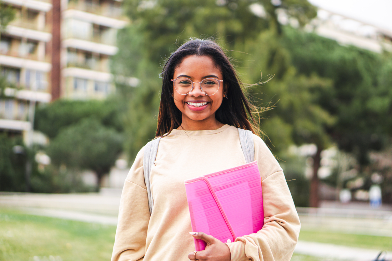 A student holding a binder and smiling cheerfully